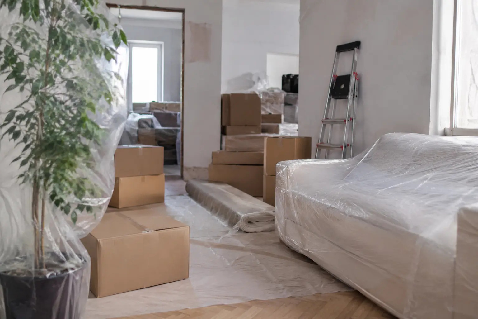Salon en travaux avec meubles sous film plastique et cartons empilés dans un logement en rénovation en Gironde